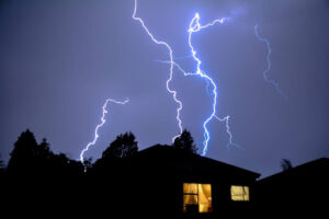 Lightning striking behind a house at night.