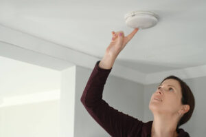 A woman testing a smoke detector in a home.