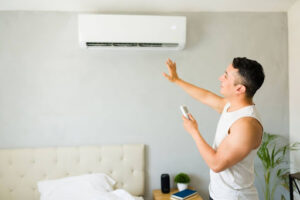 A man holding a remote and feeling the air blowing from a ductless mini-split unit in a home.