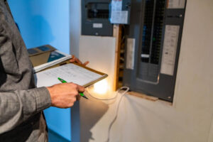 A man holding a clipboard and pen while inspecting an electrical panel.