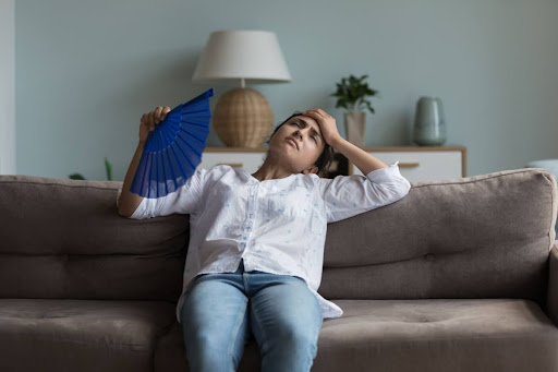 A woman fanning herself on a couch in a home.